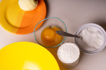 Ingredients for homemade pie stand on the table. Flour, sugar, chopped apples and egg. Close-up.