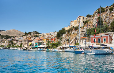 Fototapeta na wymiar Symi port, Dodecanese islands, Greece, Europe; the picturesque waterfront line of Symi town with beautiful Greek houses and colorful buildings; small sailing yachts in harbor