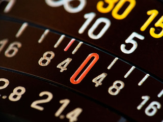 Extreme close up of old manual 35mm film camera lens with focus ring scale and aperture ring dial; vintage background and old technology; shallow depth of field