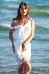 Fototapeta na wymiar Pretty woman in white wet dress posing in a sea waves