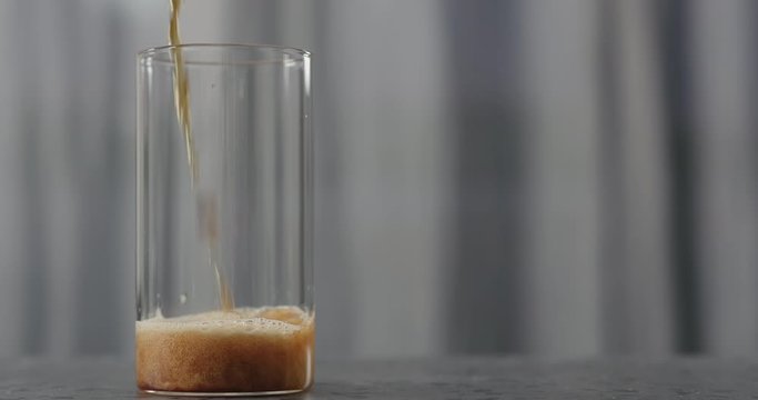 Slow motion dark beer pour into glass on concrete countertop