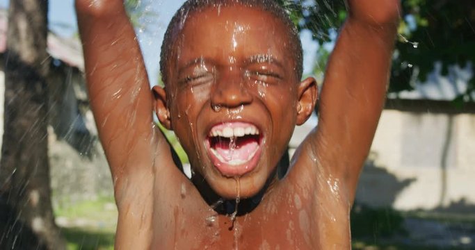 Authentic shot of happy carefree rural african little boy is having fun to play with water in a hot sunny day. Concept: freedom, charity ,life, happiness, authenticity,childhood