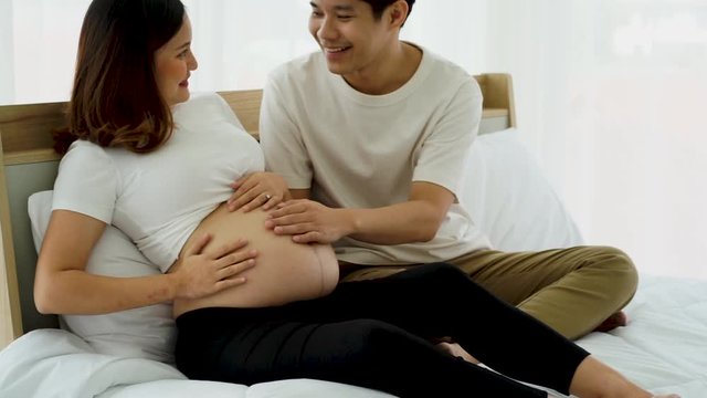 the Asian Young pregnancy woman  lay on the bed with her husband tenderness touch the bally with hands in the house 