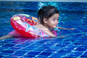 Portrait of cute little asian girl having fun in swimming pool, floating in blue refreshing water with colurful rubber ring