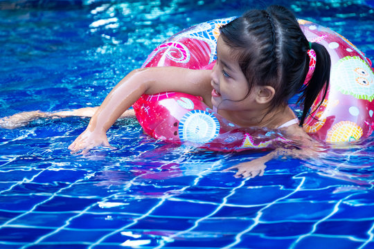 Portrait of cute little asian girl having fun in swimming pool, floating in blue refreshing water with colurful rubber ring