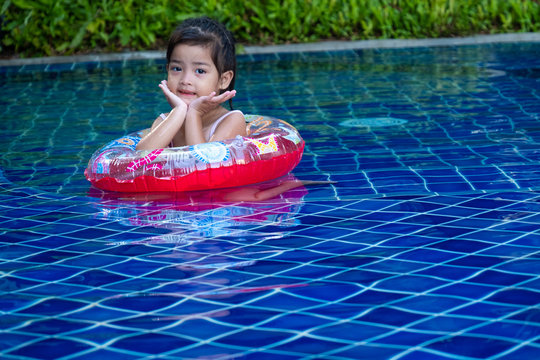 Portrait of cute little asian girl having fun and smiling in the swimming pool, floating in blue refreshing water with colurful rubber ring