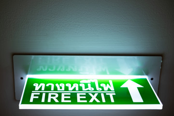 Fire exit sign in Thai and English language. Lighting is on.