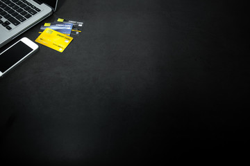 Laptop, white mobile phone and credit cards against empty dark background