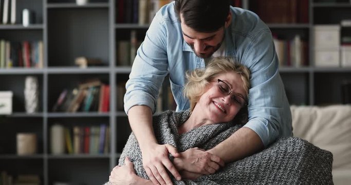 Caring grown son covering mature mother with warm plaid