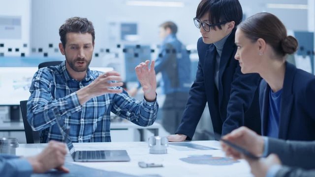 Modern Factory Office Meeting Room: Multi-Ethnic and Diverse Team of Engineers Managers Investors Talking Sitting at Table Analyzing Blueprints, Mechanism Component. High-Tech Manufactory Optimization
