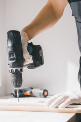 A man holds a cordless screwdriver in his hand and wraps the screw in a Board.