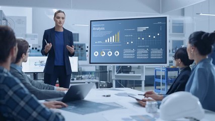 Modern Industrial Factory Meeting: Confident Female Engineer Uses Interactive Whiteboard, Makes Report to a Group of Engineers, Managers Talks and Shows Statistics, Growth and Analysis Information - Powered by Adobe