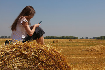 Naklejka na ściany i meble Young woman sitting on the straw bale in field
