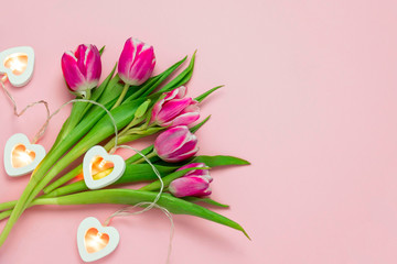 top view flat lay pink tulips and heart shaped glowing garland lights on a soft pink background with copy space