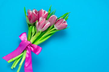 top view flat lay cute pink tulips with silk ribbon on a vibrant blue  background with copy space, spring holidays card concept