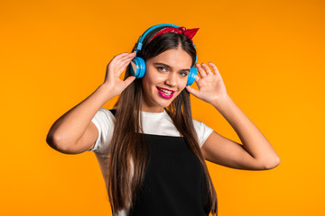 Pretty young girl with long hair having fun, smiling, dancing with headphones in studio against yellow background. Music, dance, radio concept,
