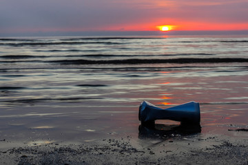 A drink can was thrown on the seashore during the beautiful sunrise.