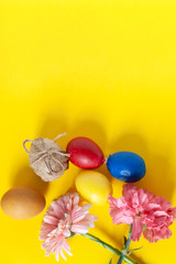 Colorful easter eggs with bright colorful spring flowers on the yellow background. Top view. View from directly above. Spring festive holidays background. Vertical image