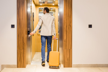 Rear view of modern man with baggage getting in hotel or office building elevator.