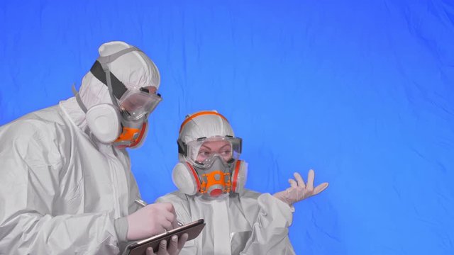 Scientist virologist in respirator makes write in an tablet computer with stylus. Man and woman wearing protective medical mask. Health safety virus coronavirus epidemic 2019 nCoV. Chroma key blue.
