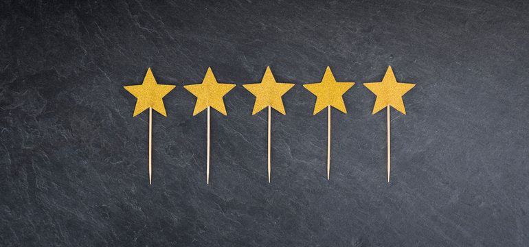 Five golden stars on slate background as symbol for rating