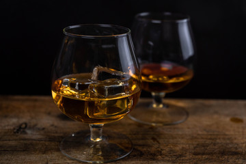 Two whiskey / cognac glasses with ice on a wooden background. Dark backdrop.
