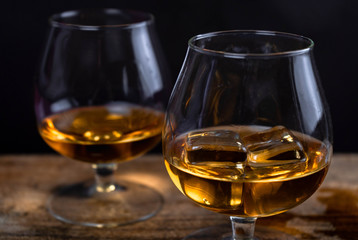 Two whiskey / cognac glasses with ice on a wooden background. Dark backdrop.