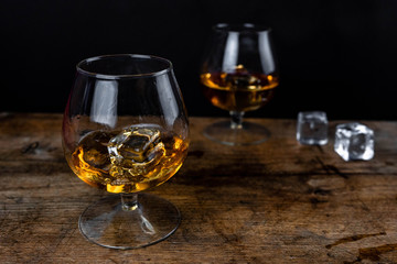Two whiskey / cognac glasses with ice on a wooden background. Dark backdrop.