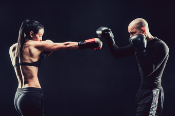Shirtless Woman exercising with trainer at boxing and self defense lesson, studio, dark background....