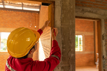 Plasterer in red working uniform check balance of wood window frame, check center byTry Square