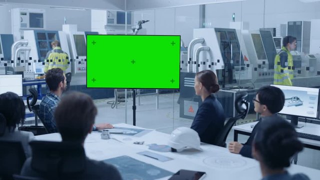 Modern Factory Office Room: Diverse Team of Engineers, Managers and Investors Sitting at Meeting Table, They wave at Interactive TV that shows Green Screen Video Call Conference