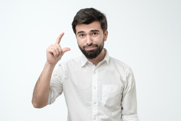 Fototapeta premium Hispanic handsome pitiful guy showing less gesture salary income savings. Studio shot