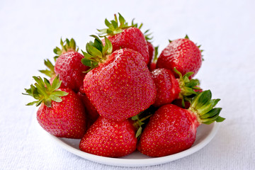 Ripe sweet red strawberries in a white bowl on a white towel