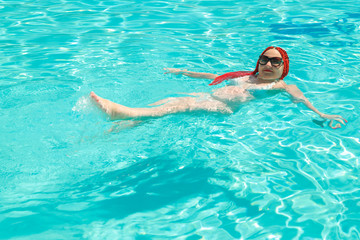 A woman with African pigtails swims on her back in the pool.