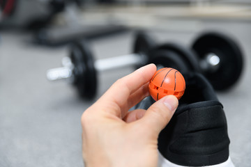 Hand holding shoe freshener ball in front of athlete footwear and dumbells. Concept for avoiding unpleasant smell or odor from training shoes, sneakers and general footwear in an active lifestyle.