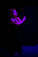 Woman in the image of the devil on a black background in purple lighting in full growth.