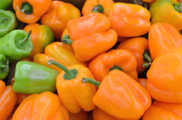 Orange peppers background at the food market, orange and green sweet peppers in a pile, raw vegan food, ripe vegetables