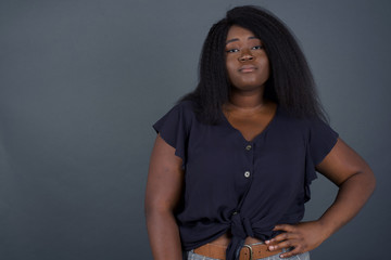 Studio shot of cheerful African American woman keeps hand on hip, smiles broadly, anticipates for surprise prepared by friends on her birthday, isolated over gray background.