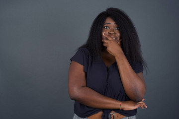 Anxiety - a conceptual image of a beautiful young African American woman covering her mouth with her hands and standing indoors. Scared from something or someone bitting nails