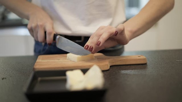 Close up of woman hands cutting fresh parmesan cheese in slices on a wodden board. Female manicured hands cutting a parmesan into sticks on a little cutting board