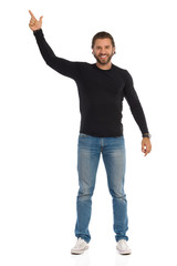 Handsome Man Is In Black Blouse And Jeans Is Standing And Pointing Up. Front View.