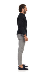 Handsome Man In Gray Trousers, Moccasins And Black Shirt Is Standing Relaxed And Looking Away. SIde...