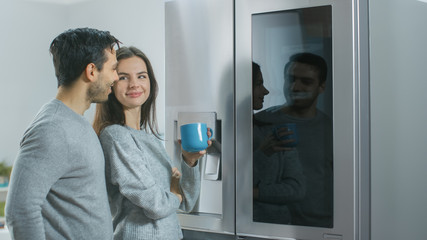 Beautiful Young Couple Drink Morning Coffee in the Kitchen. They Check the Weather Forecast and a...