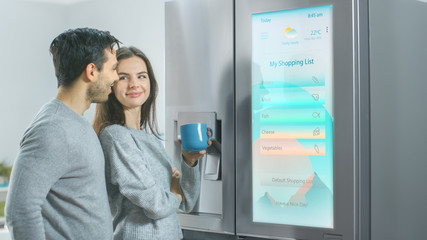 Beautiful Young Couple Drink Morning Coffee in the Kitchen. They Check the Weather Forecast and a...