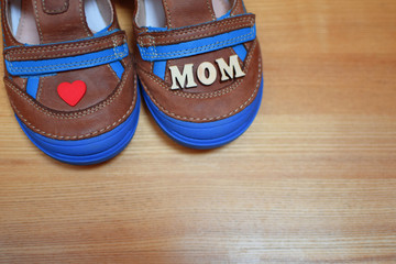 Brown leather children boy's shoes with blue soles and little red heart and word mom on light wooden background with copy space. Happy mother's day concept. I love mom.