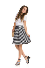 Young Woman In Striped Skirt And High Heels Is Posing With Straw Purse And Looking Away.
