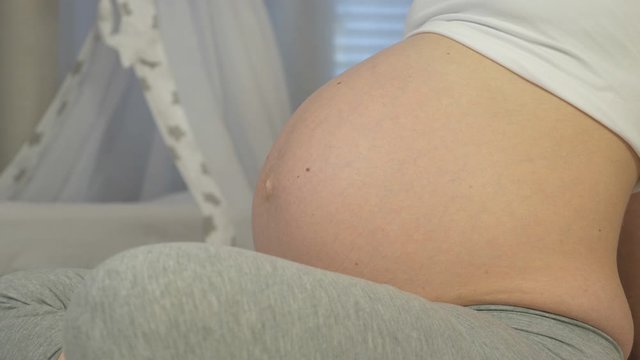 Pregnant woman sits on the bed and listens to unborn baby kicking in her belly. Young woman in last month of pregnancy. Baby moves in the mother's stomach