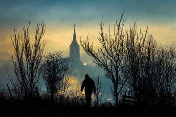 Man silhouette walking towards misty village landscape seen from above - obrazy, fototapety, plakaty