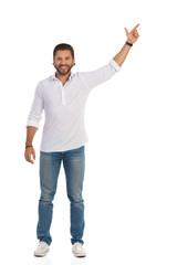 Handsome Young Man Is Standing With Arm Raised, Pointing Up And Smiling