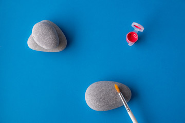 Flat lay, top view of the table. Different artist brushes and sea pebbles for painting with red paint on a blue background. copy space